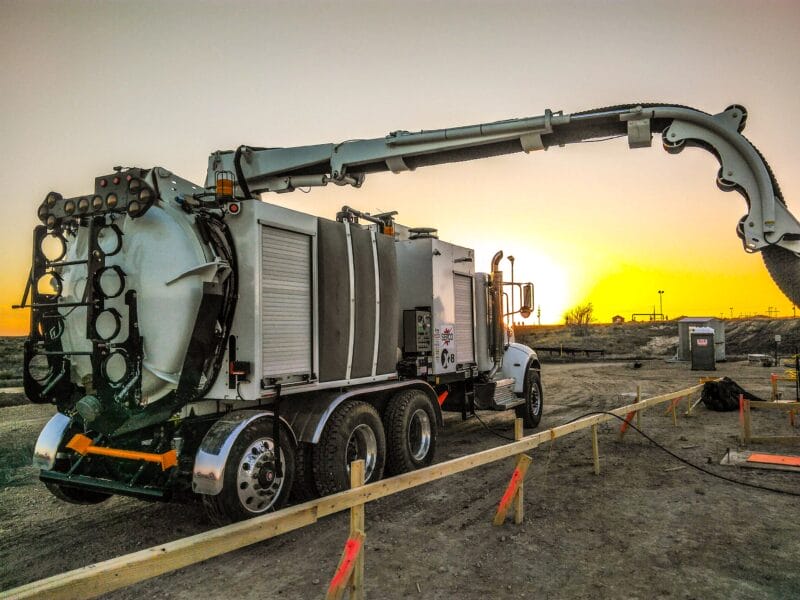 White X-Vac hydro-excavation truck with articulated boom extended at sunset on a construction site